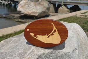 Inlay of Nantucket Island on a wooden oval sitting on a rock with harbor in the background.